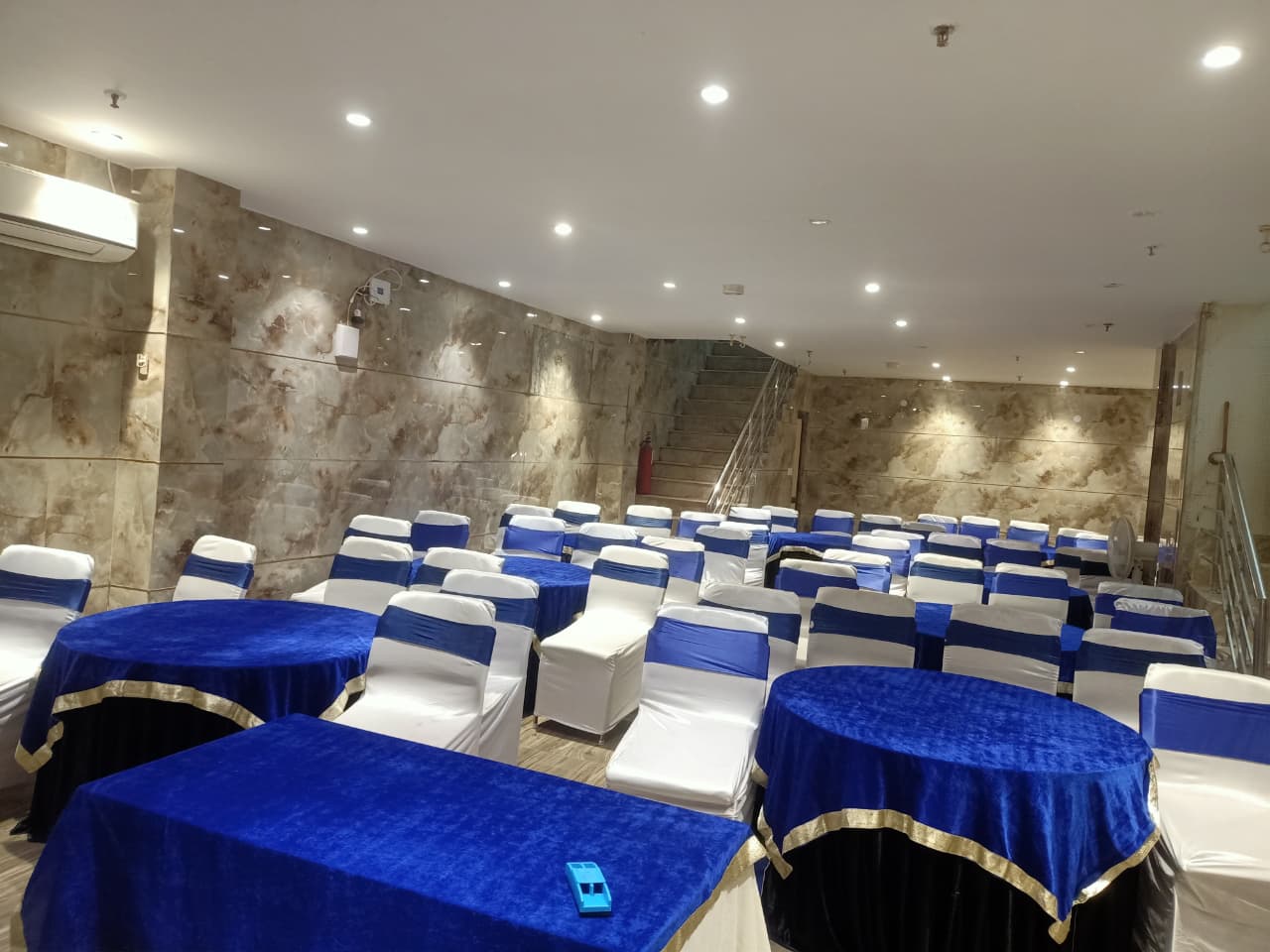 Conference hall arranged with blue banquet tables and seating near the staircase